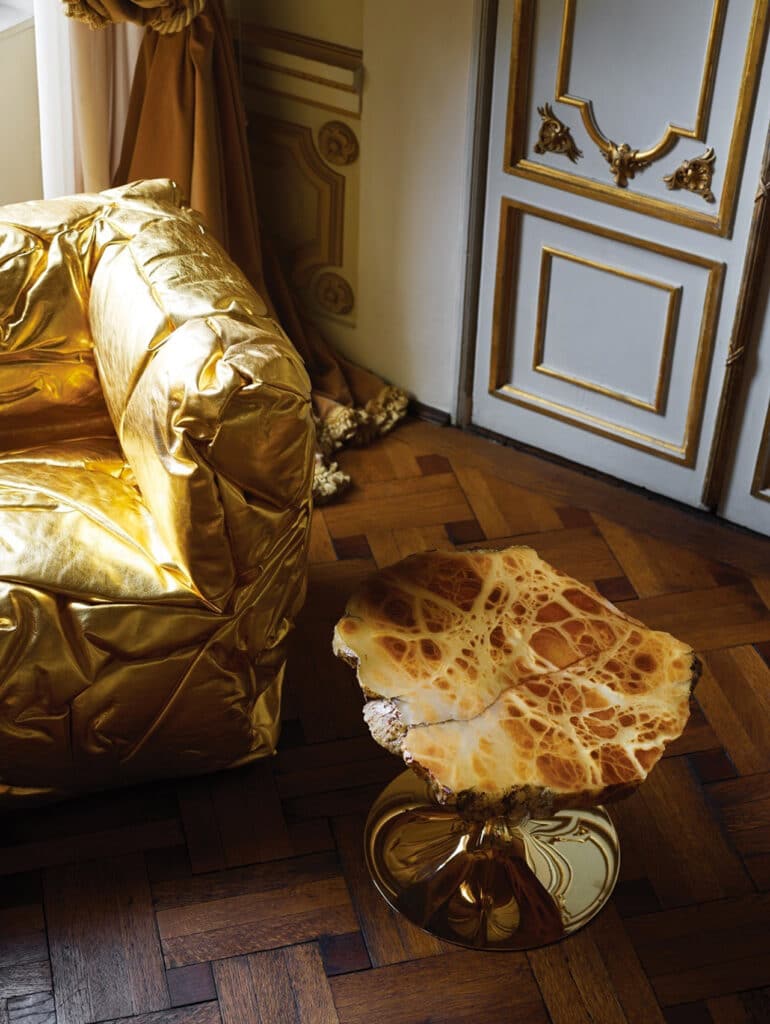 Hier zien we de Sponge-armchair in een luxe setting, gecombineerd met een bijzettafel met marmer blad. De gouden uitvoering benadrukt het sculpturale karakter en de artistieke visie van Peter Traag. Deze presentatie laat zien hoe de stoel kan worden geïntegreerd in een ruimte die zowel klassiek als artistiek is.