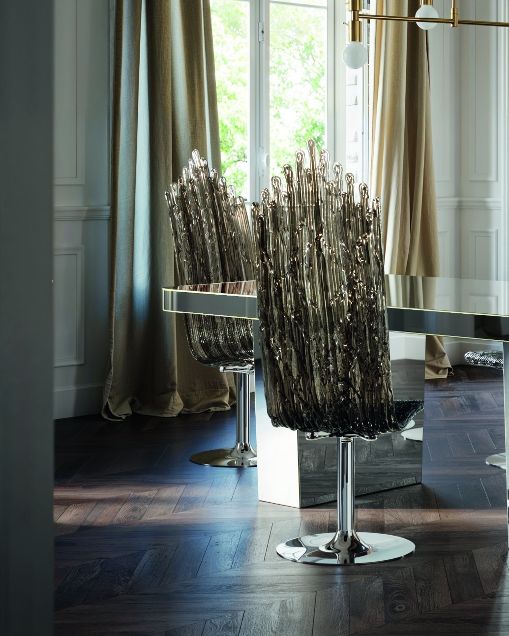 De Milano-stoelen van Edra staan stijlvol geplaatst bij een moderne spiegeltafel in een verfijnde eetkamer. De transparante, geribbelde rugleuningen vangen het licht en creëren een subtiele schittering, wat een luxueuze uitstraling aan de stoelen geeft. De chromen basis van de stoelen voegt een modern accent toe dat perfect past bij de glanzende tafel en het warme houten vloerpatroon. Deze setting onderstreept de veelzijdigheid van de Milano-stoelen als luxueuze designstukken die moeiteloos in een stijlvol interieur passen