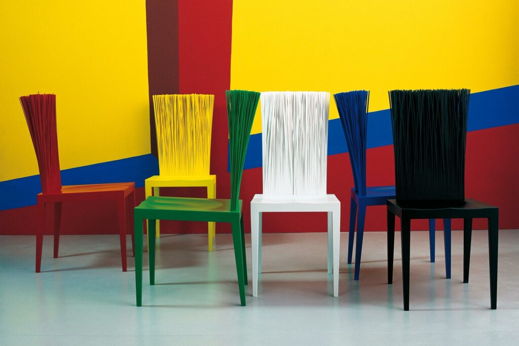 Een kleurrijke opstelling van Edra Jenette-stoelen in rood, geel, groen, wit, blauw en zwart tegen een speelse achtergrond. Deze presentatie toont de veelzijdigheid en esthetische kracht van het ontwerp.