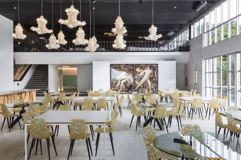 Een ruim en stijlvol restaurant waarin de Gina stoelen van Edra een speelse, moderne twist toevoegen aan de inrichting. De stoelen met amberkleurig polycarbonaat materiaal vullen de ruimte perfect aan onder de imposante kroonluchters, wat zorgt voor een chique en artistieke sfeer.