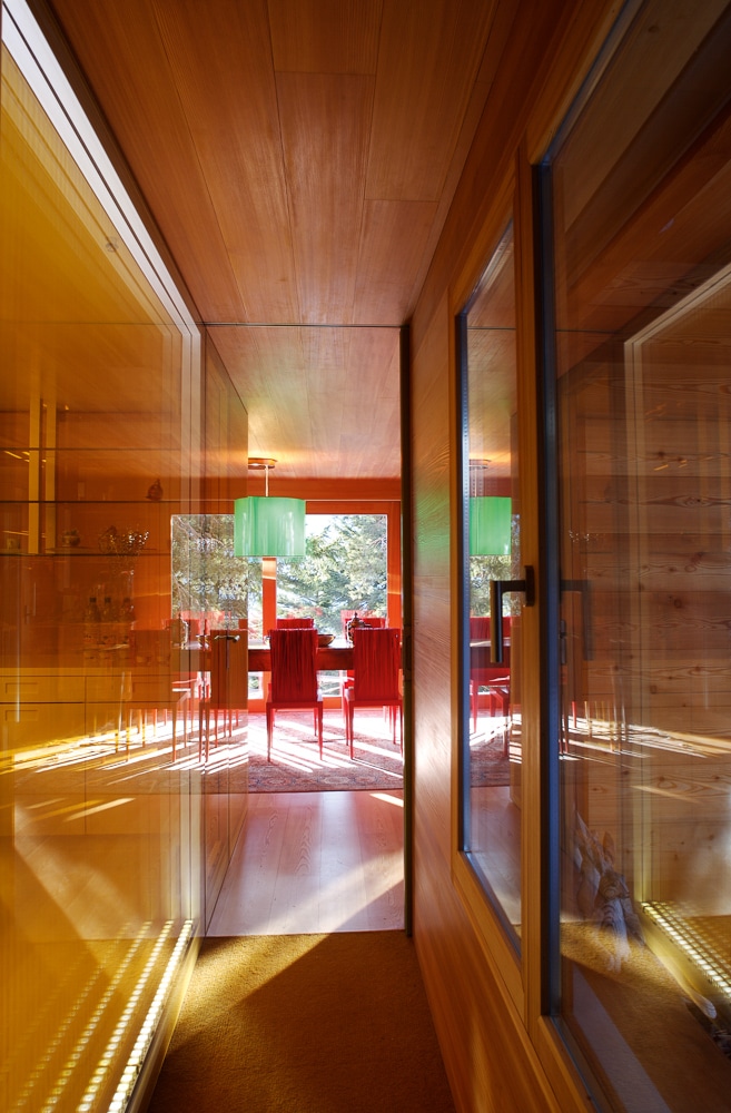 Een houten gang leidt naar een eetkamer waar meerdere rode Jenette-stoelen van Edra rond een tafel staan. Het warme licht en de rode accenten creëren een uitnodigende sfeer