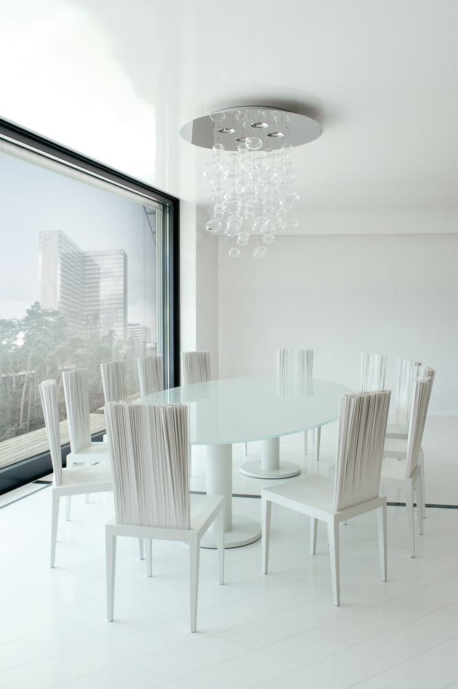 Een lichte en open eetkamer met witte Jenette-stoelen van Edra rond een glazen tafel. De minimalistische inrichting straalt rust en verfijning uit