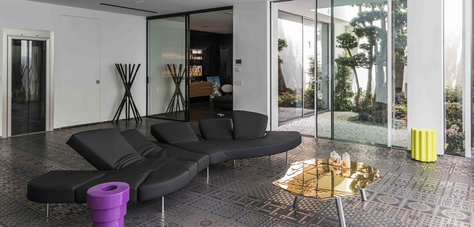 Een Brasilia tafel met een gouden glasmozaïek tafelblad, gecombineerd met een zwarte loungebank in een luxe interieur. Het tafelblad reflecteert het licht en creëert een warme en uitnodigende sfeer.